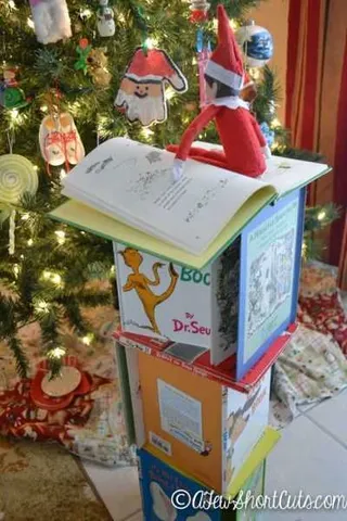 Elf On A Shelf Building Tower Of Books To Decorate Tree